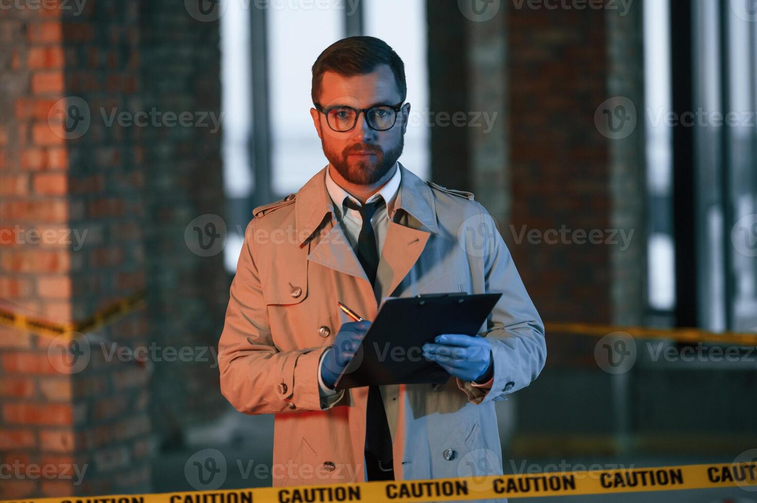 Male detective i,n coat is collecting evidence in a crime scene on the construction site. With notepad in hands photo