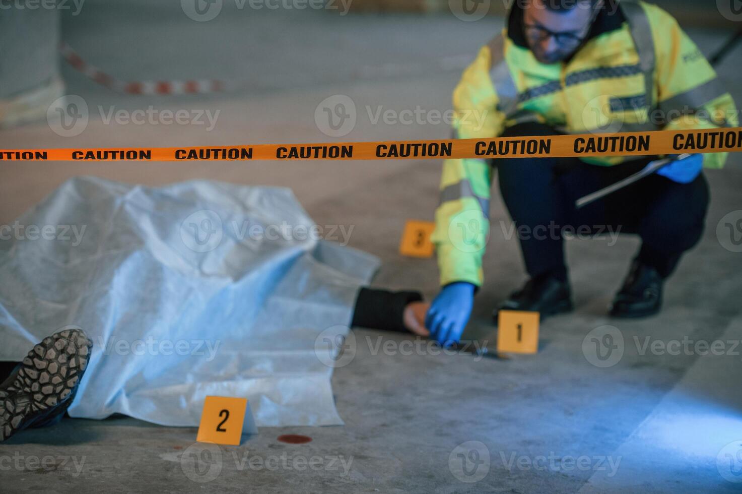 Knife is on the floor. Male detective is collecting evidence in a crime scene near dead body on the construction site photo