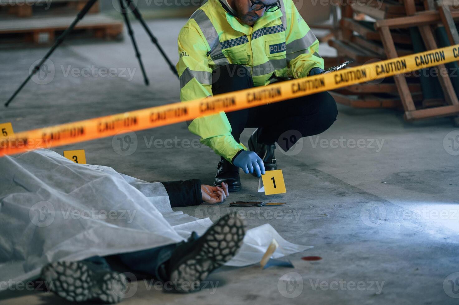 Knife is on the floor.. Male detective is collecting evidence in a crime scene near dead body on the construction site photo