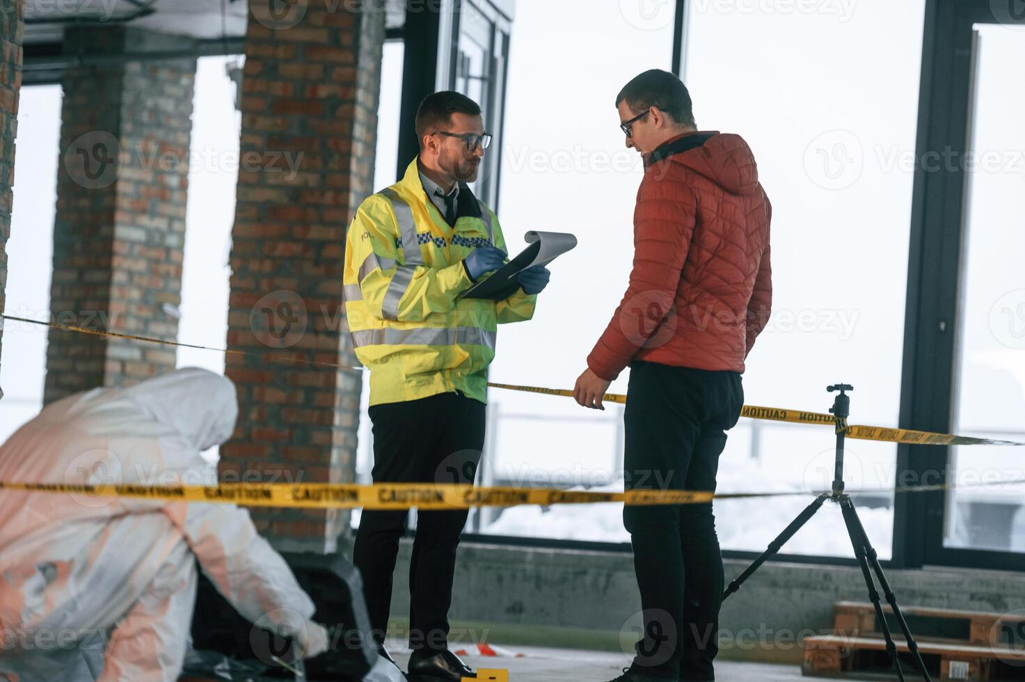The ,witness is being questioned. Two detectives are collecting evidence in a crime scene photo
