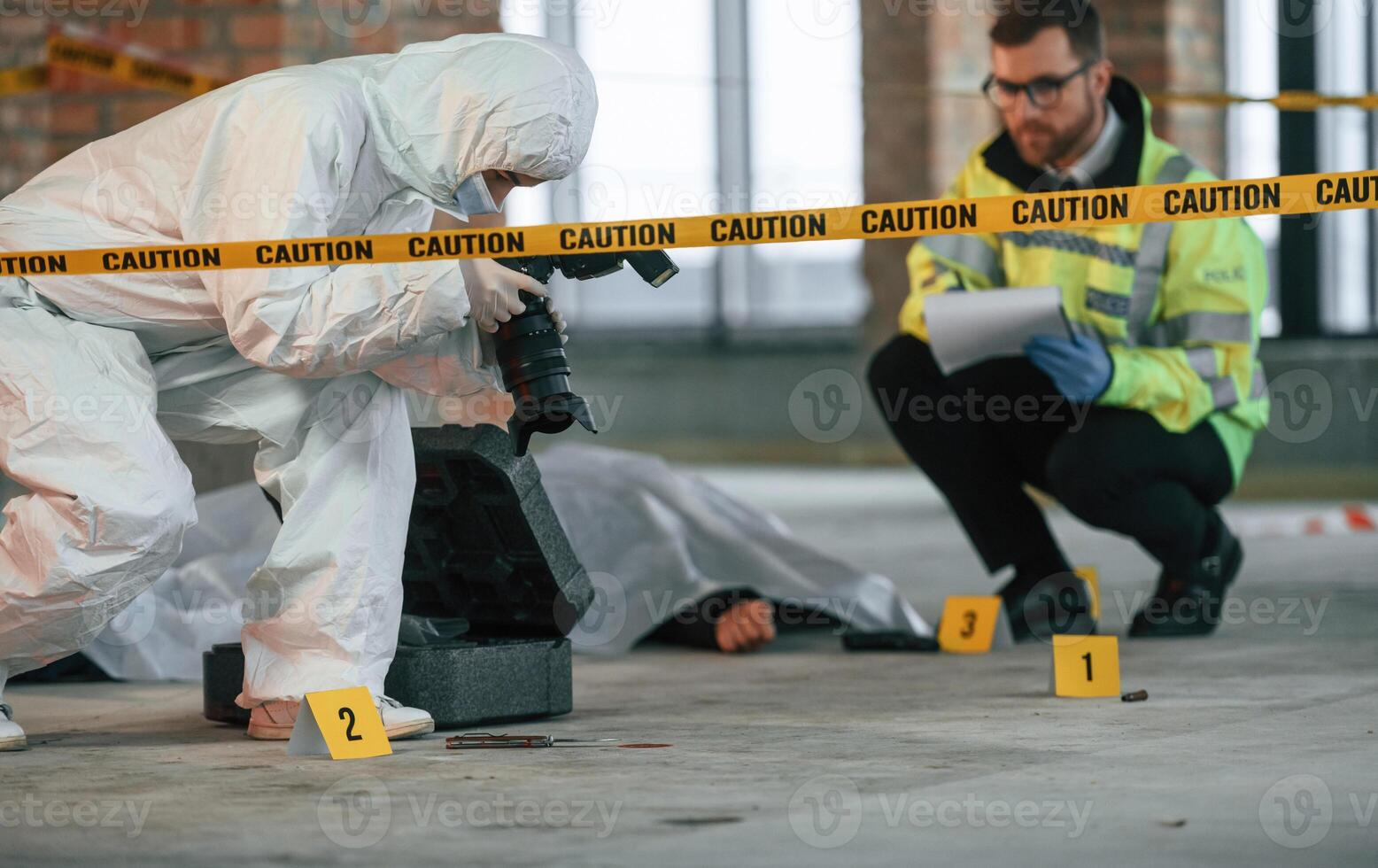 Woman is making photos by camera. Detectives are collecting evidence in a crime scene near dead body