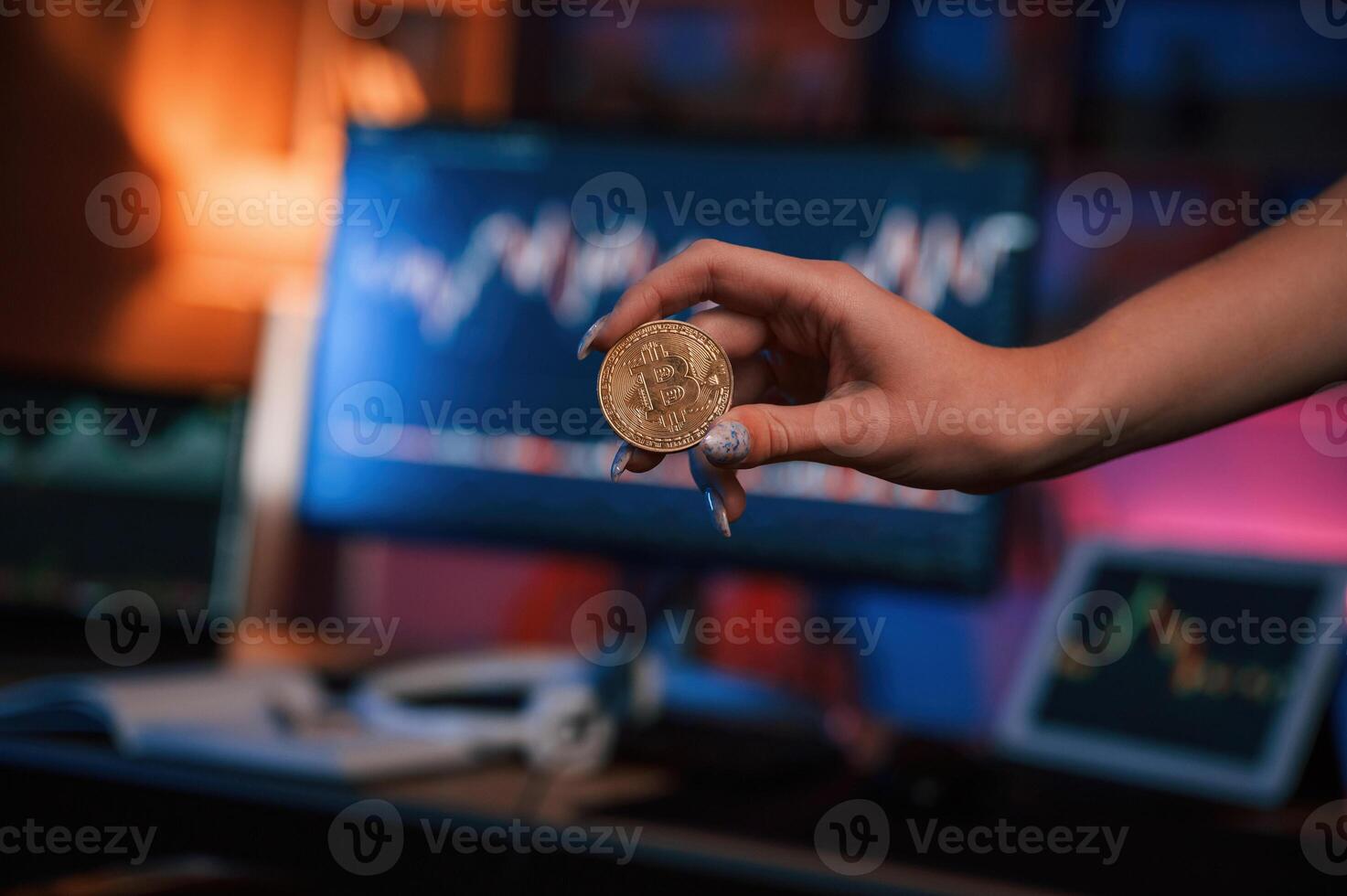 Close up view of woman's ,hand that holding bitcoin against computer display and tablet with graphs photo