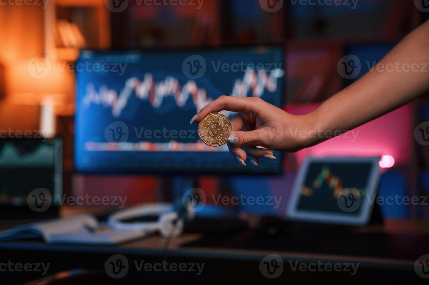 Close up view of woman's hand, that holding bitcoin against computer display and tablet with graphs photo
