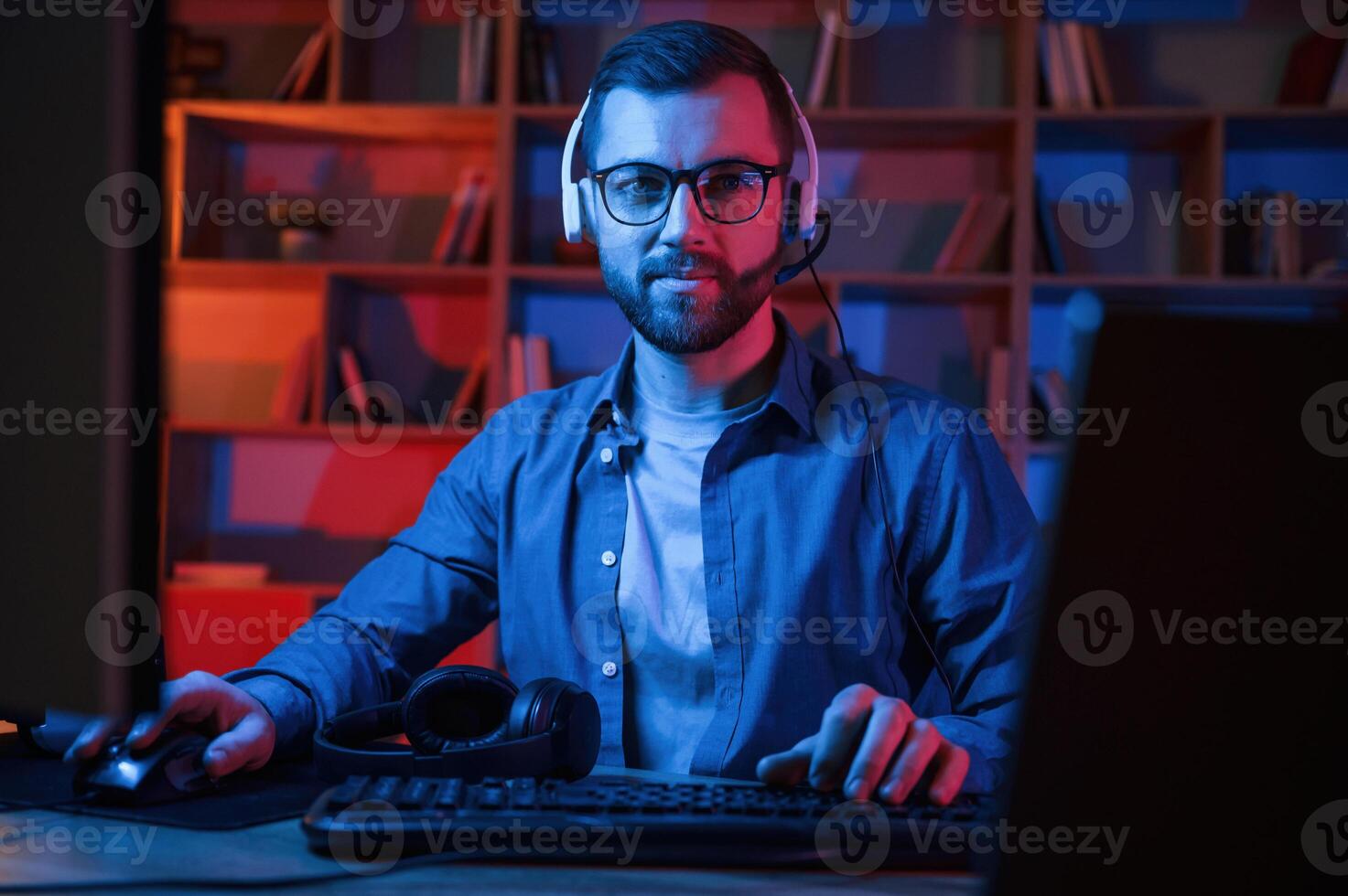 Concentrated man is sitting by, a computer indoors at home. Neon lighting photo