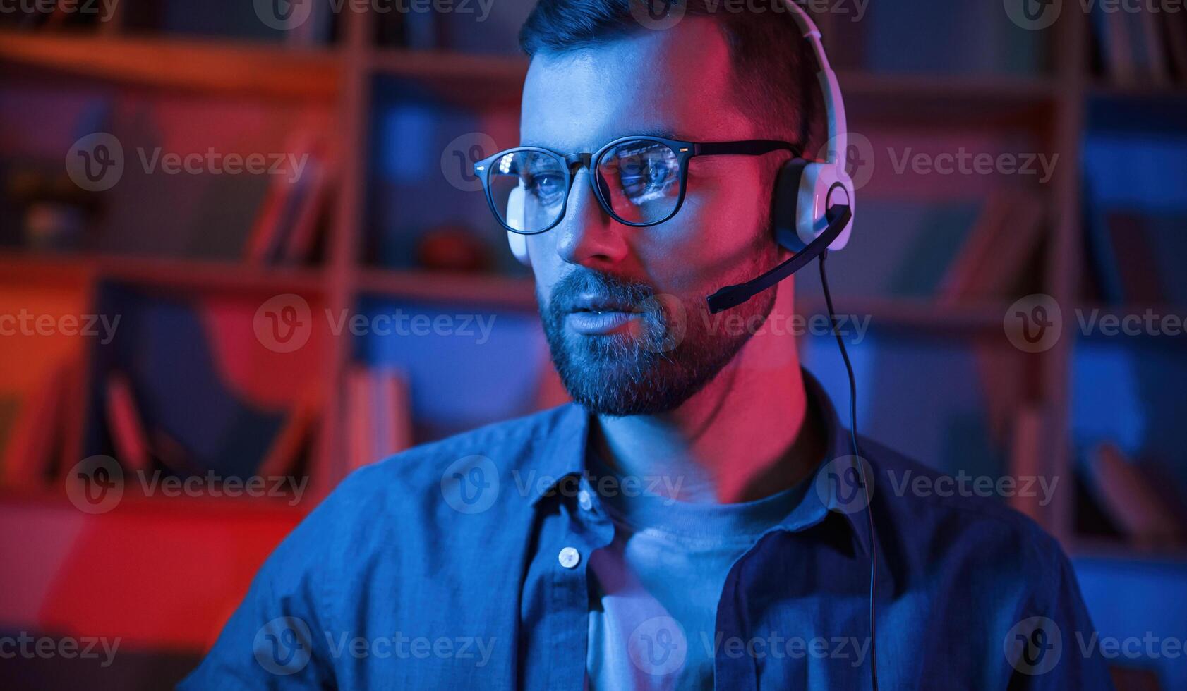 Portrait of man that, is sitting by a computer indoors at home. Neon lighting photo