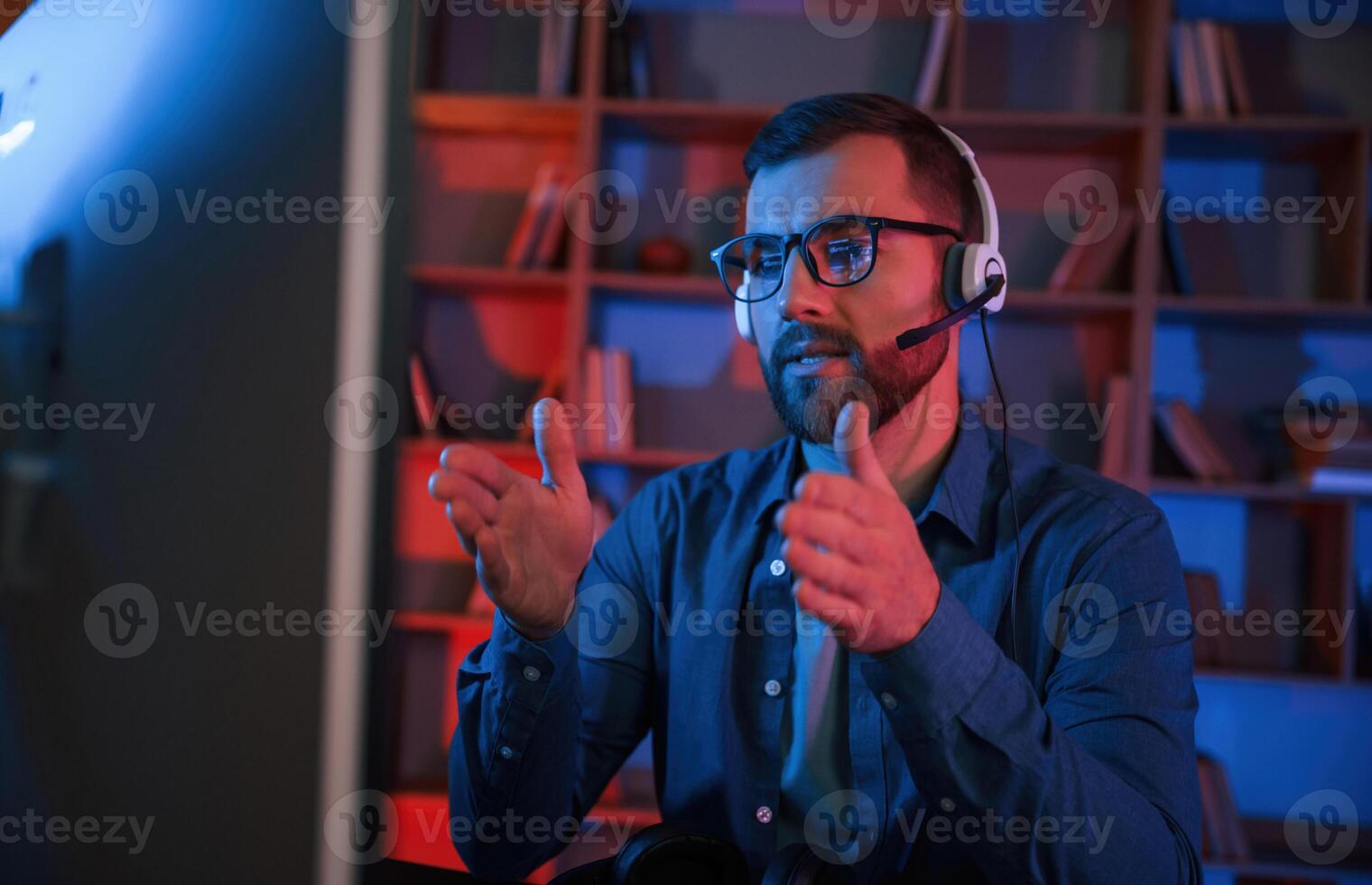 Concentrated man is sitting, by a computer indoors at home. Neon lighting photo