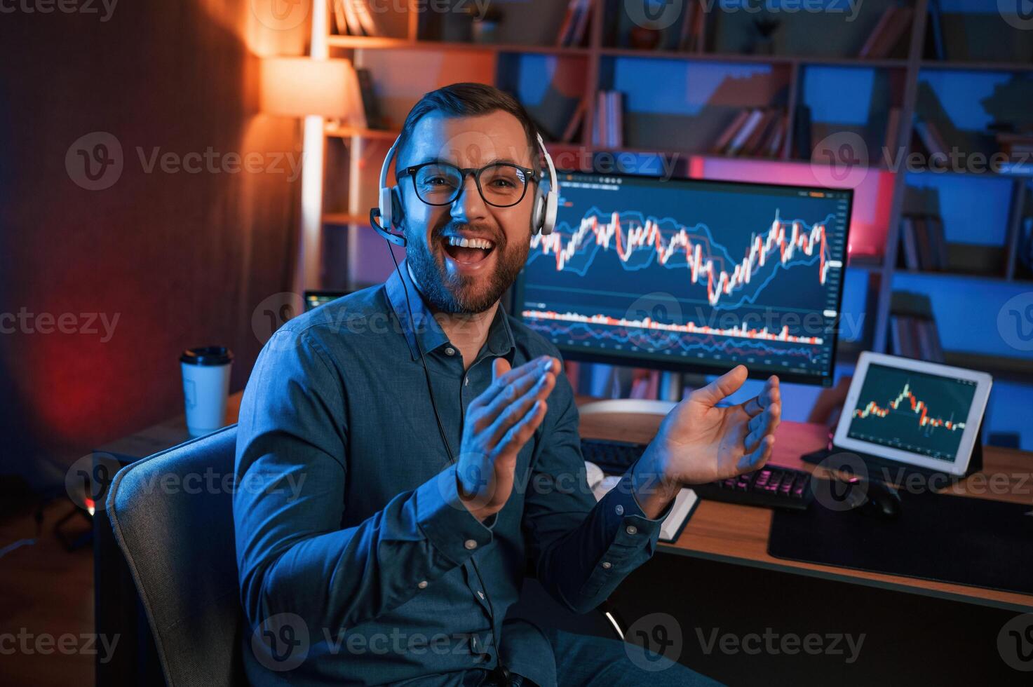Sitting and, looking at the camera. Stock trader is working by pc indoors. Conception of exchange and money photo