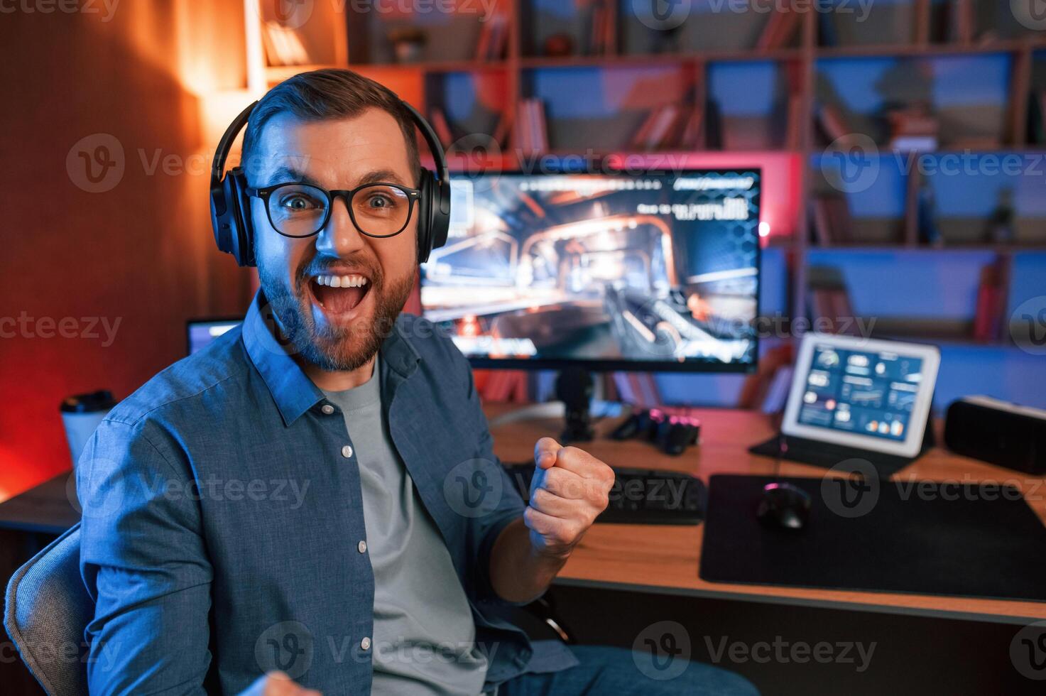 Celebrating victory. Man ,is playing the shooter game on his computer. Neon lighting photo