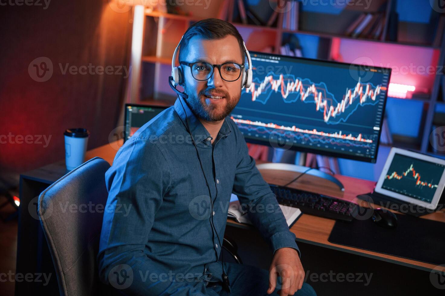Sitting, and looking at the camera. Stock trader is working by pc indoors. Conception of exchange and money photo