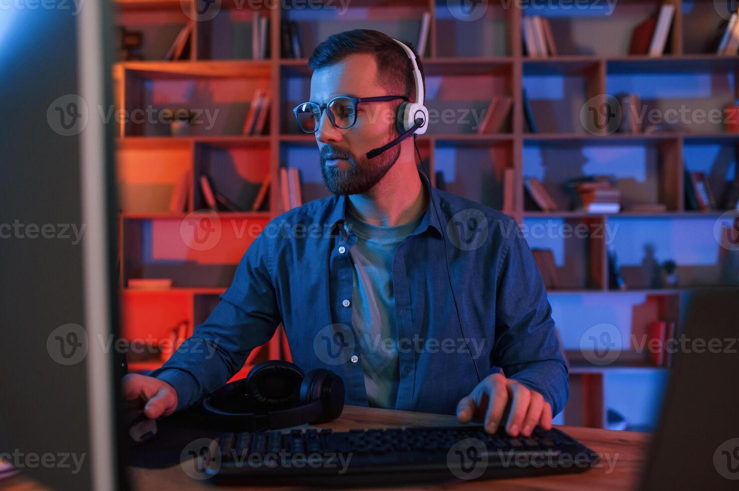 In glasses. Man is sitting by a computer, indoors ,at home. Neon lighting photo