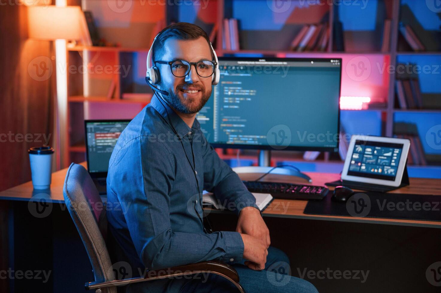 Positive professional programmer is working, indoors and smiling. Neon lighting photo