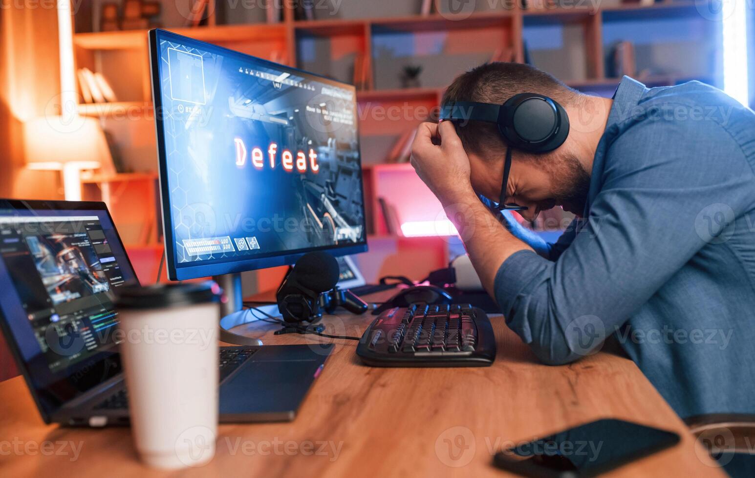 Conception of defeat. Man is playing the shooter game on his computer. Neon lighting photo