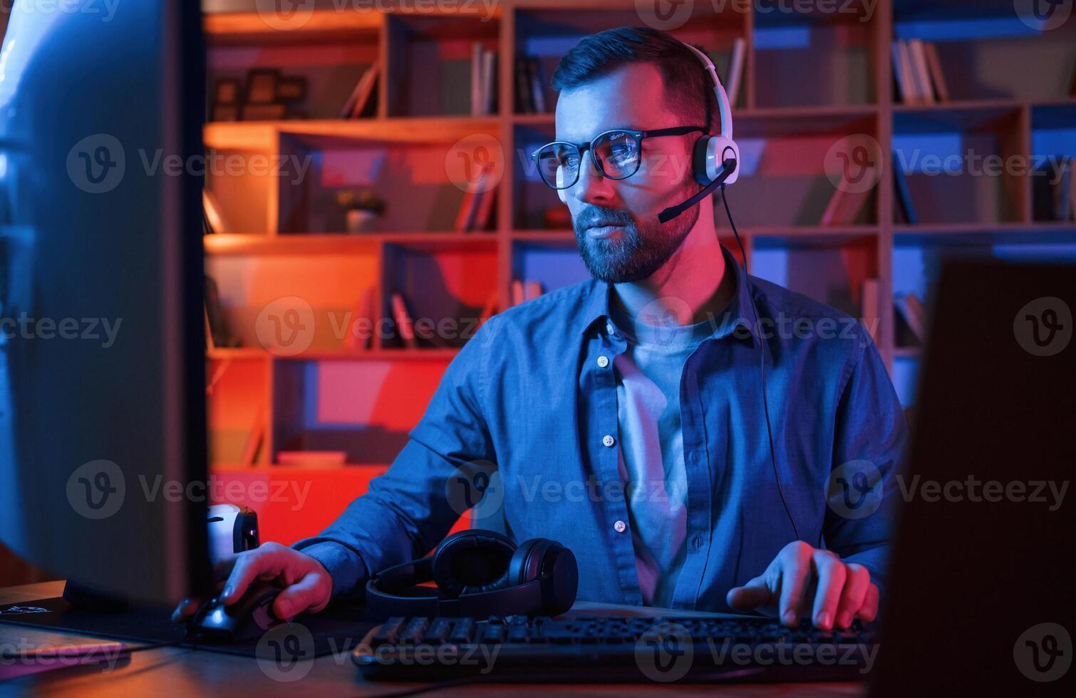 Concentrated man is sitting by a computer indoors at home. Neon lighting photo