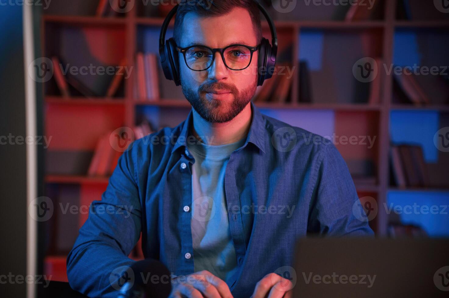 In glasses. Man is sitting ,by a computer indoors at home. Neon lighting photo