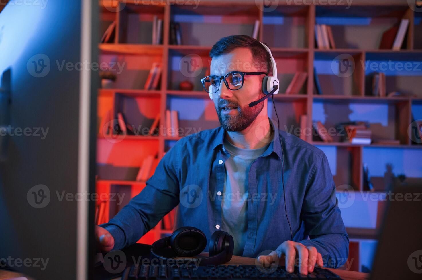 Having, online meeting. Man is sitting, by a computer indoors at home. Neon lighting photo