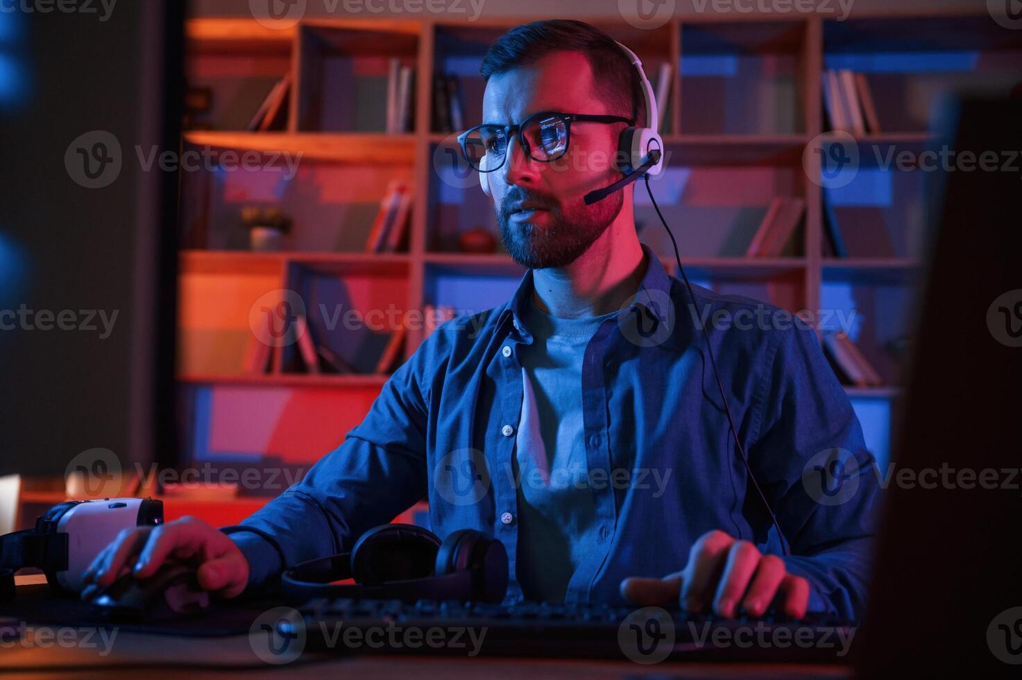 Front view.. Man is sitting by a computer indoors at home. Neon lighting photo