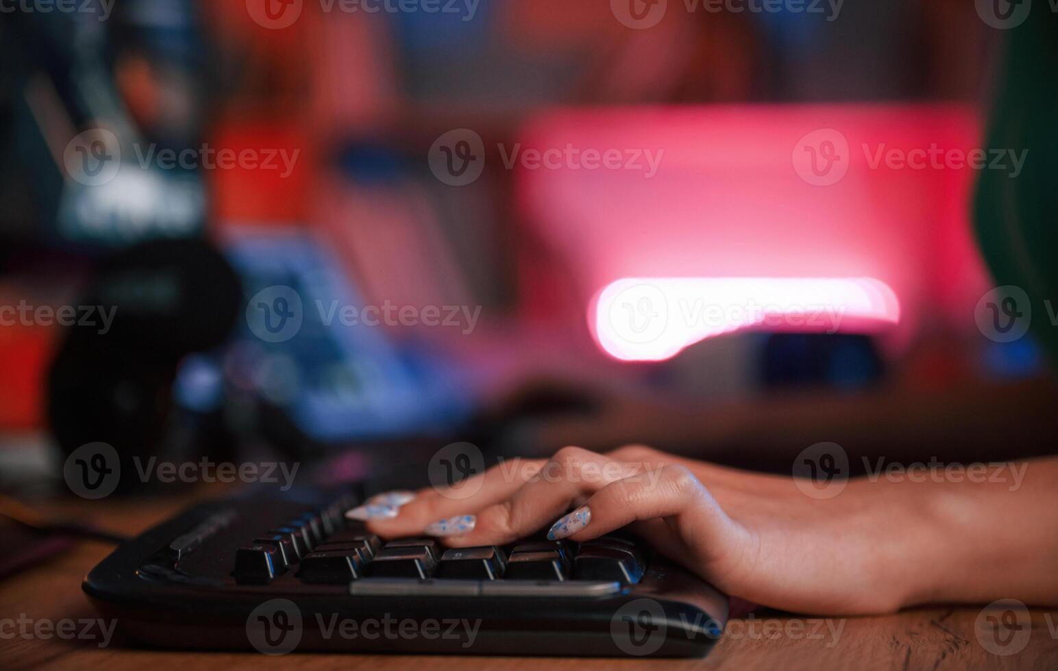 Close up view of woman's hand that is typing on the keyboard in dark room with neon lighting photo
