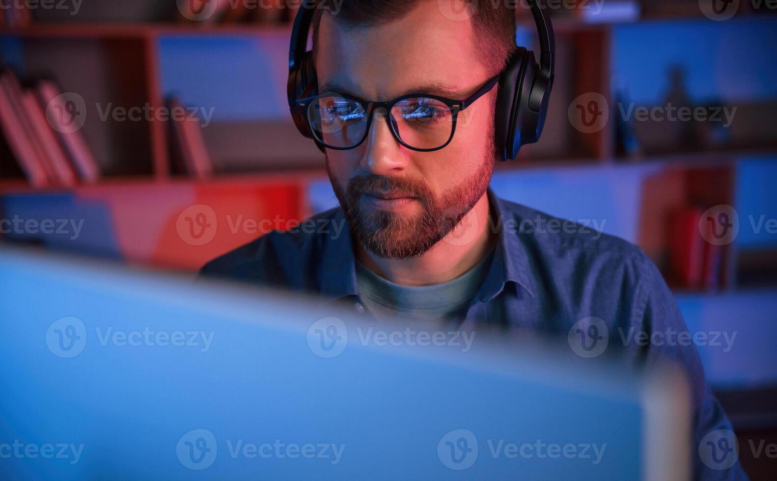 Front view. Man is sitting by a computer indoors at home. Neon lighting photo