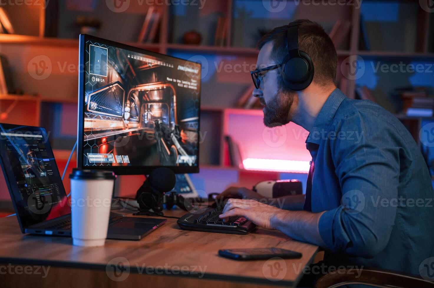 Concentrated man is playing the shooter game on, his computer. Neon lighting photo