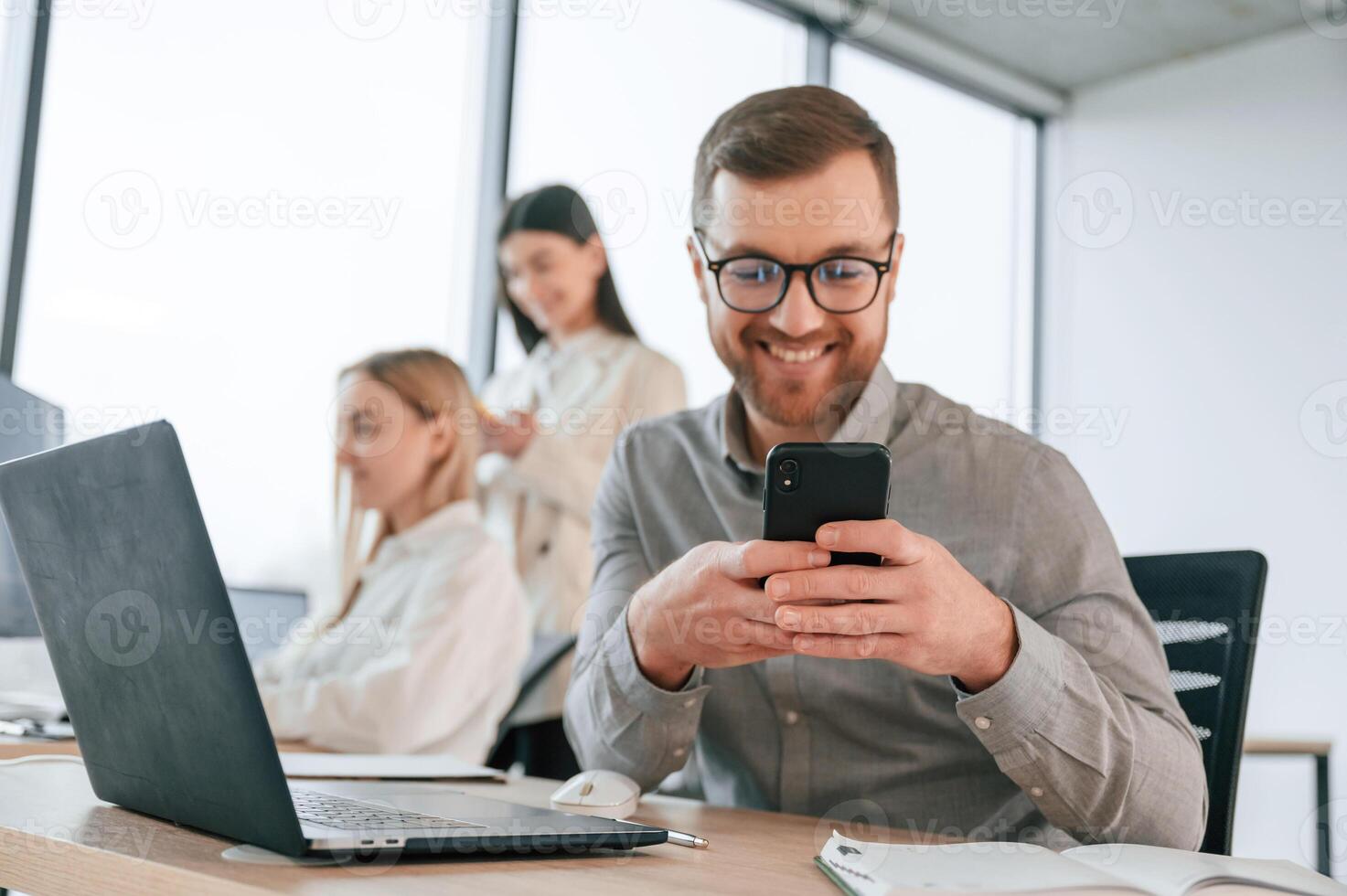 Smiling and holding, smartphone. Successful team are working together in the office. Conception of business photo