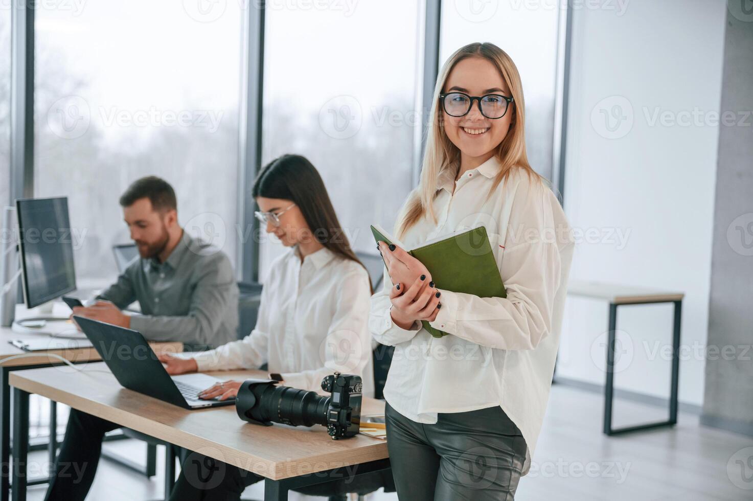 Woman in glasses is standing with notepad ,in hands. Successful team are working together in the office photo