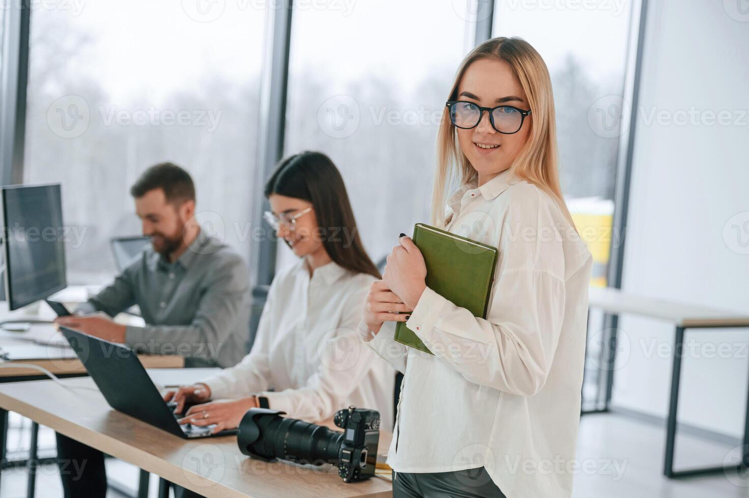 Woman in ,glasses is standing with notepad in hands. Successful team are working together in the office photo