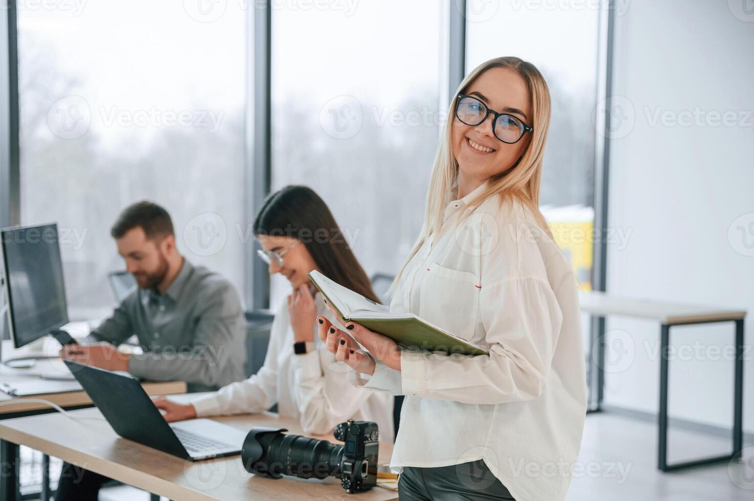 Womanm in glasses, is standing ,with notepad in hands. Successful team are working together in the office photo