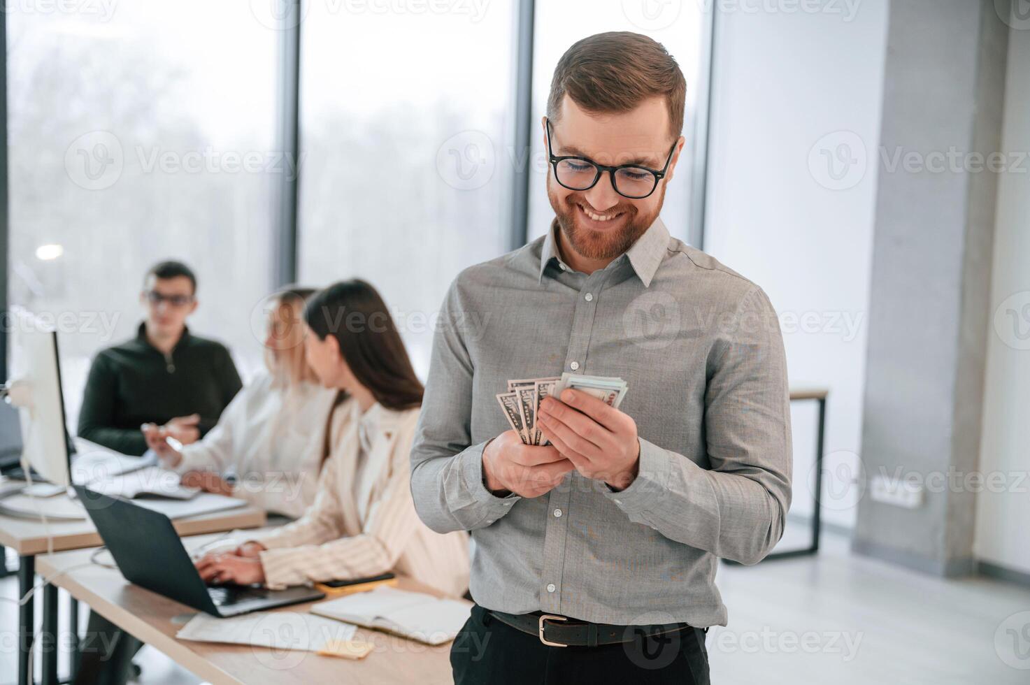 Man is holding money in hands.. Successful team are working together in the office. Conception of business photo
