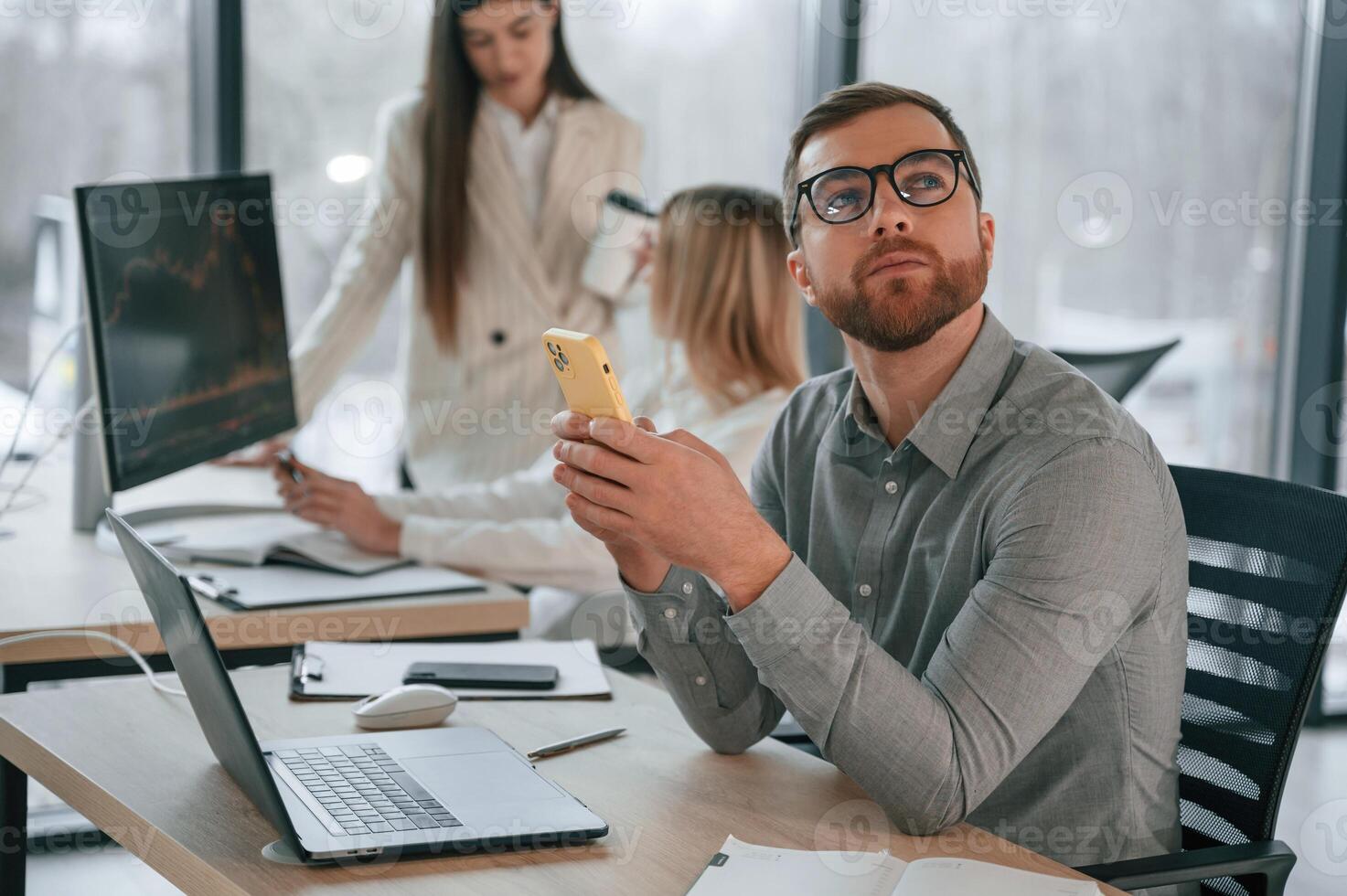 Man is sitting and using smartphone. Successful team are working together in the office. Conception of business photo