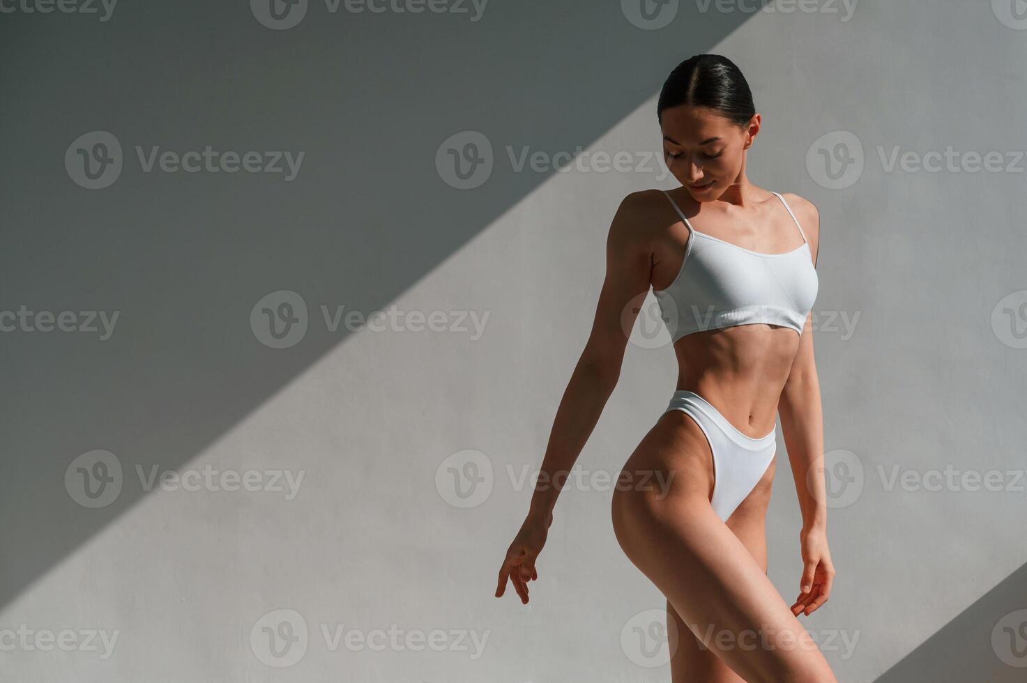 Standing against ,the wall and showing body. Young caucasian woman is indoors in the studio photo