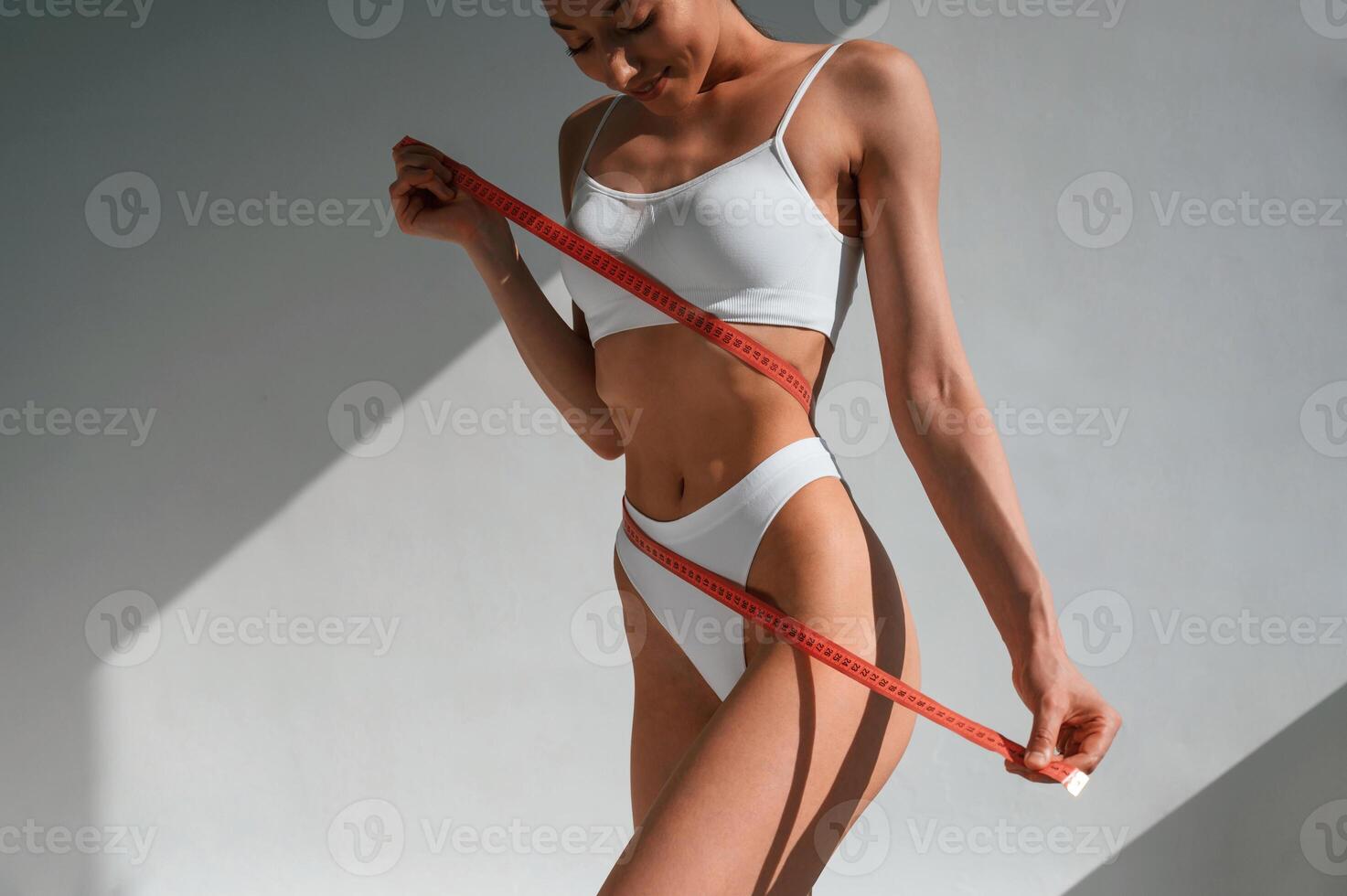 Measuring tape in hands. Young caucasian woman with slim body shape is indoors in the studio photo