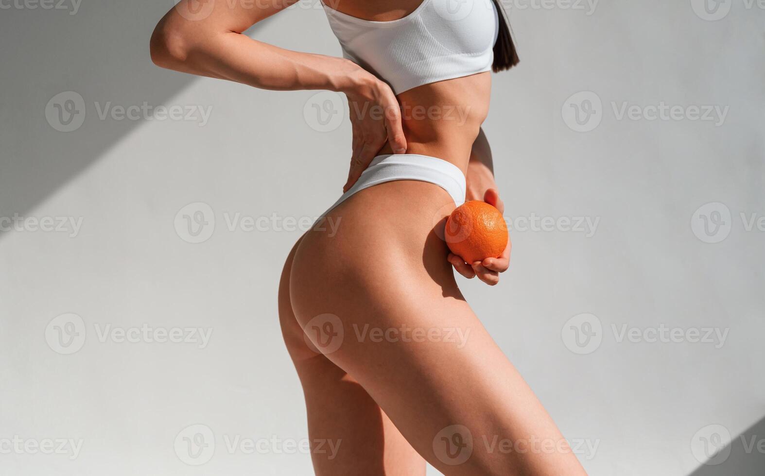 With an orange in hand. Young caucasian woman with slim body shape is indoors in the studio photo