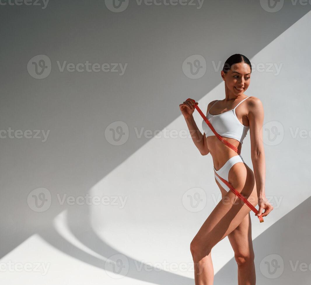 Measuring ,tape ,in hands. Young caucasian woman with slim body shape is indoors in the studio photo