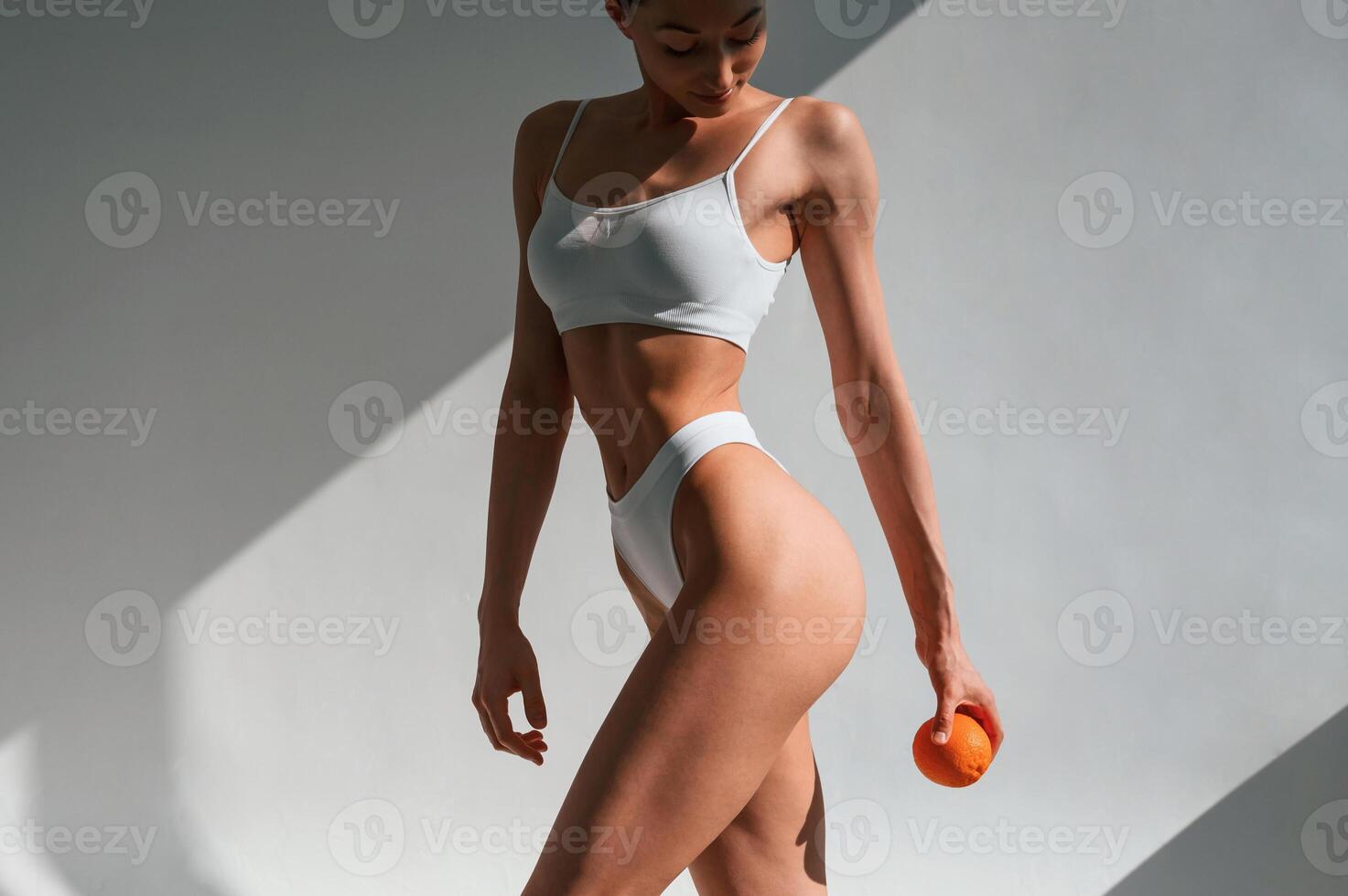 With an, orange in hand. Young caucasian woman with slim body shape is indoors in the studio photo
