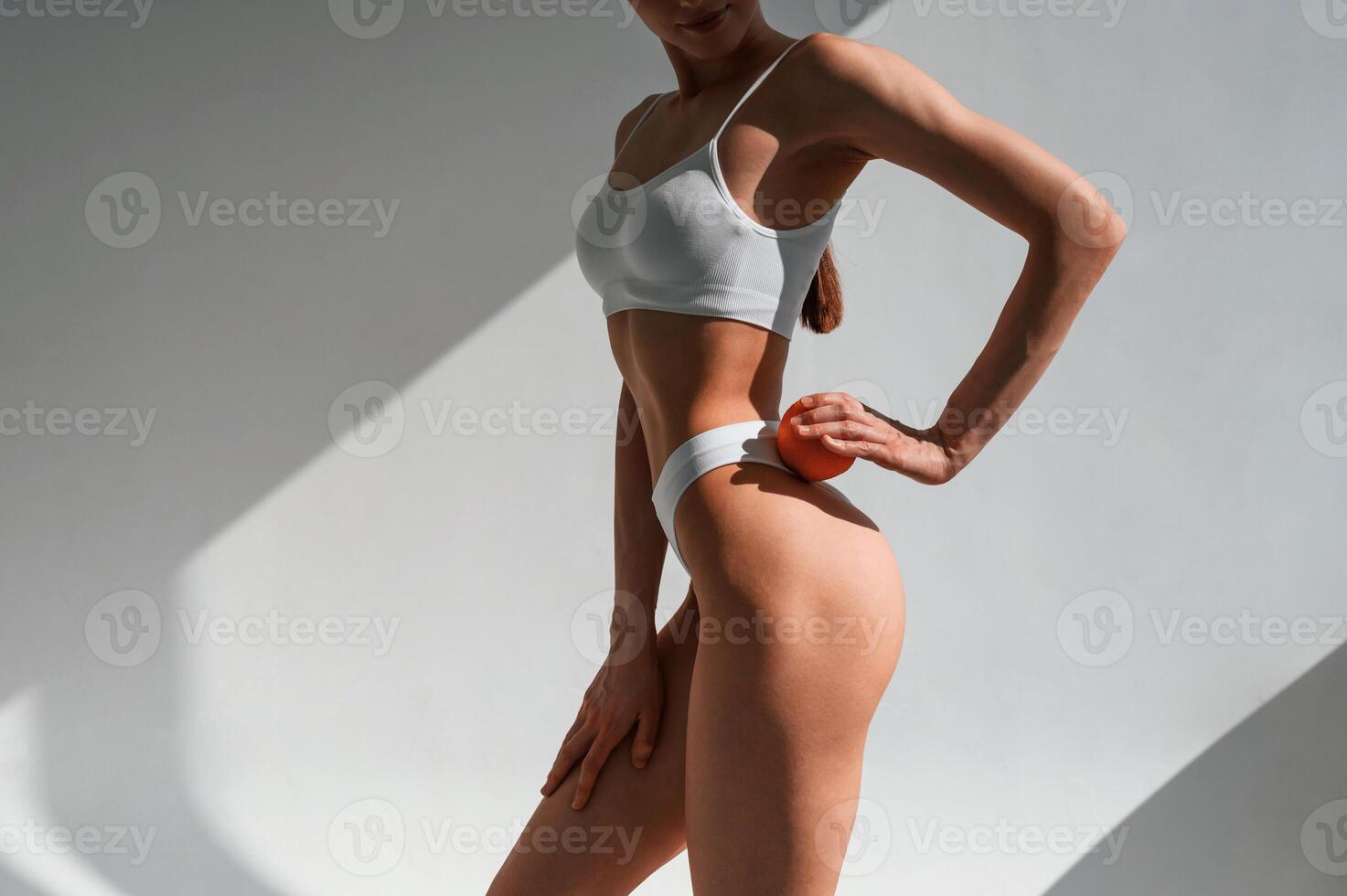 With an orange i,n hand.. Young caucasian woman with slim body shape is indoors in the studio photo