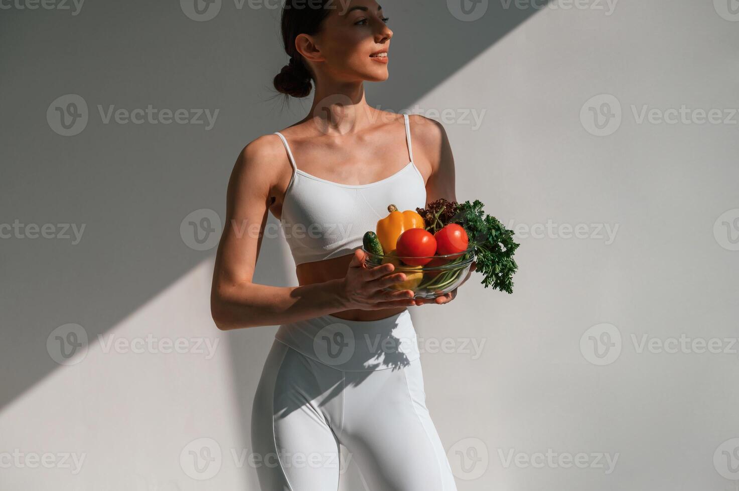 Holding, vegetables and fruits. Young caucasian woman with slim body shape is indoors in the studio photo