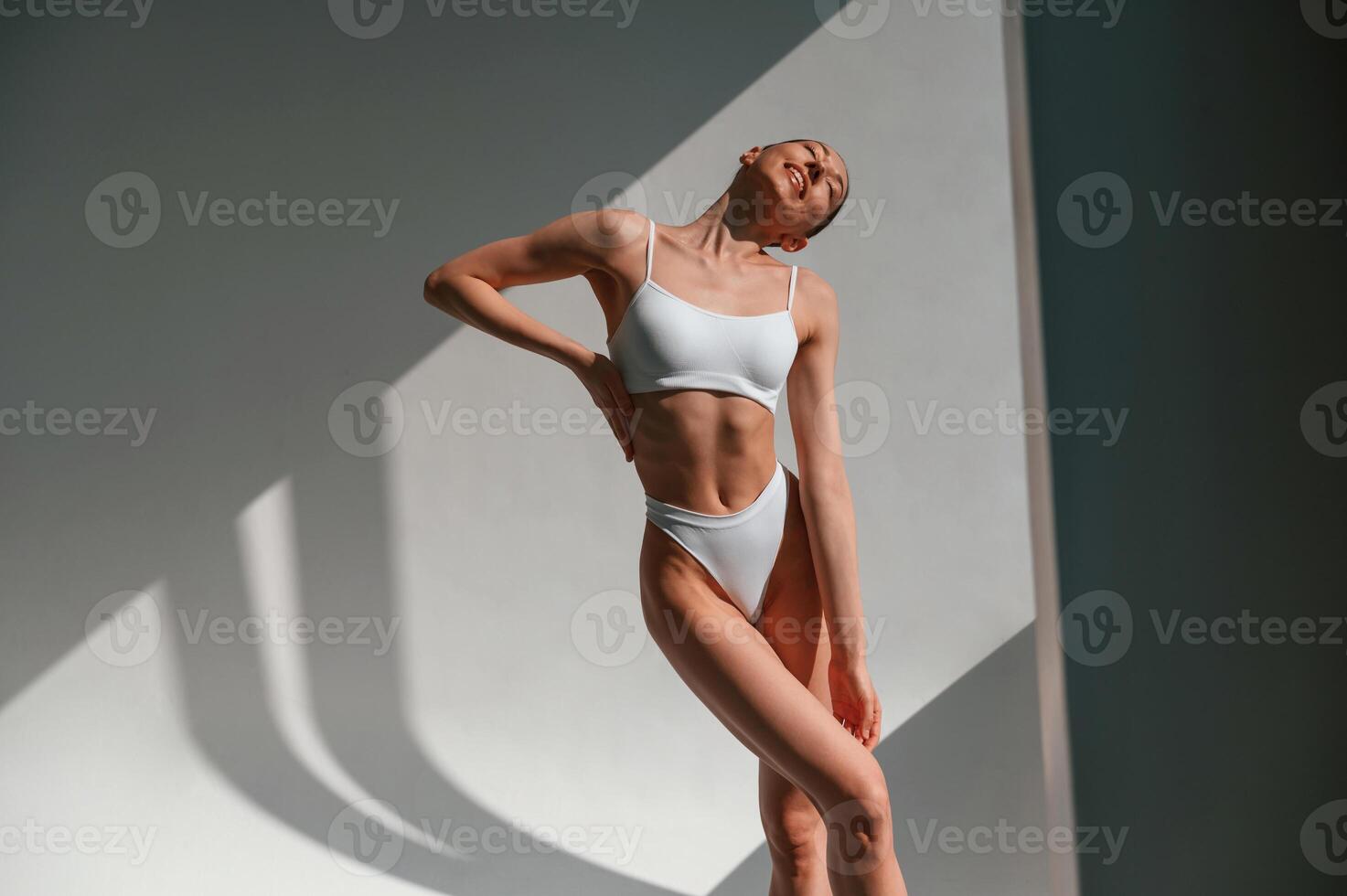 Illuminated by sunlight. Young, caucasian woman with slim body shape is indoors in the studio photo