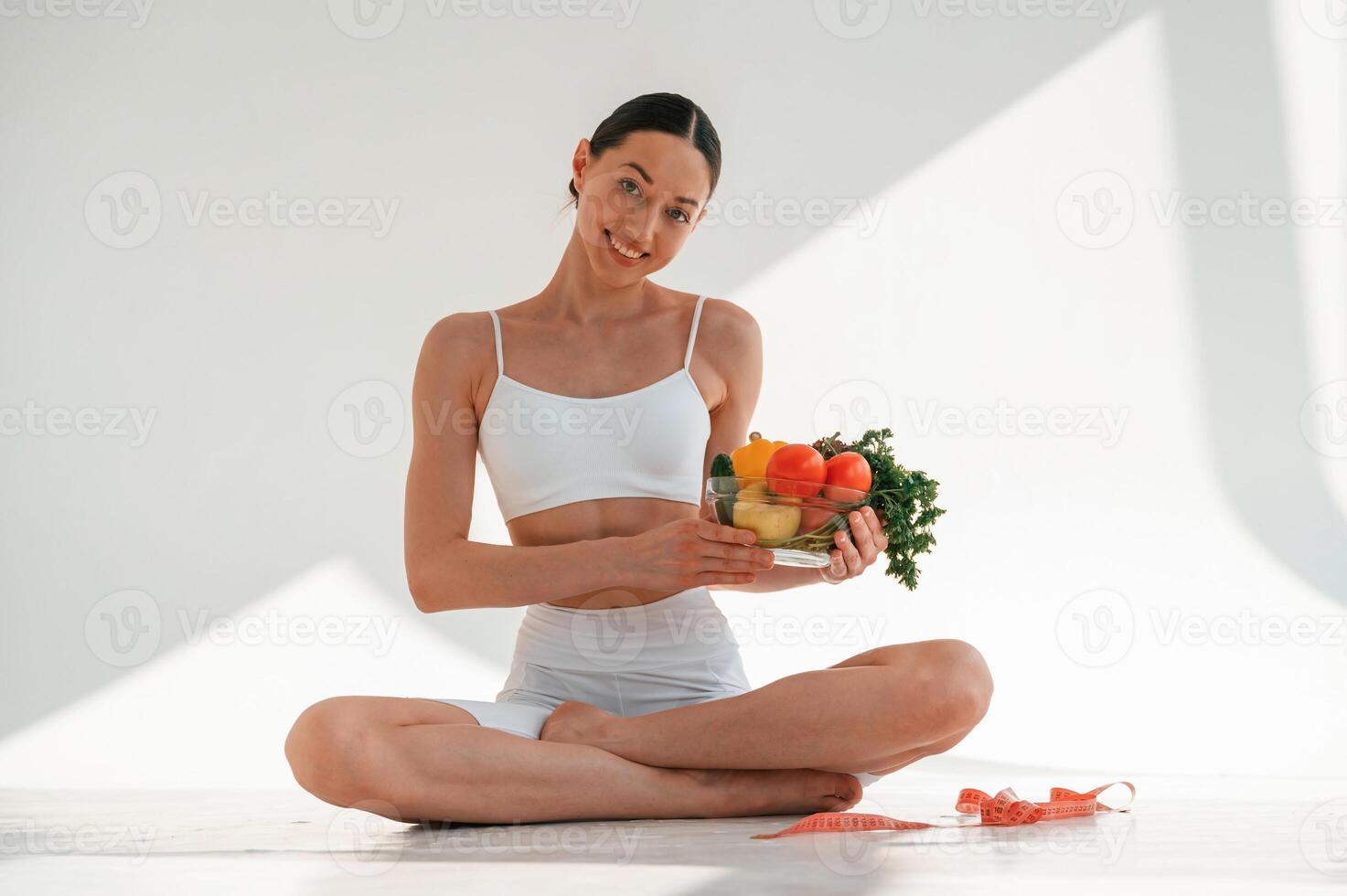 Sitting on the ,floor with healthy food. Young caucasian woman with slim body shape is indoors in the studio photo