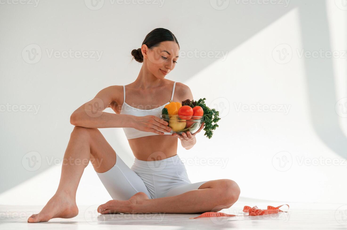 Sitting, on the, floor with healthy food. Young caucasian woman with slim body shape is indoors in the studio photo