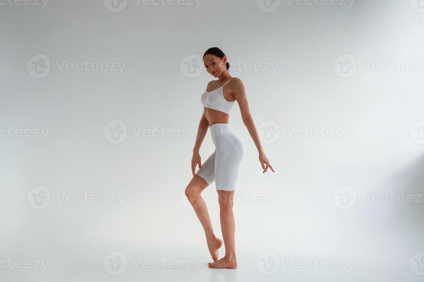 In white, fitness clothes. Young caucasian woman with slim body shape is indoors in the studio photo
