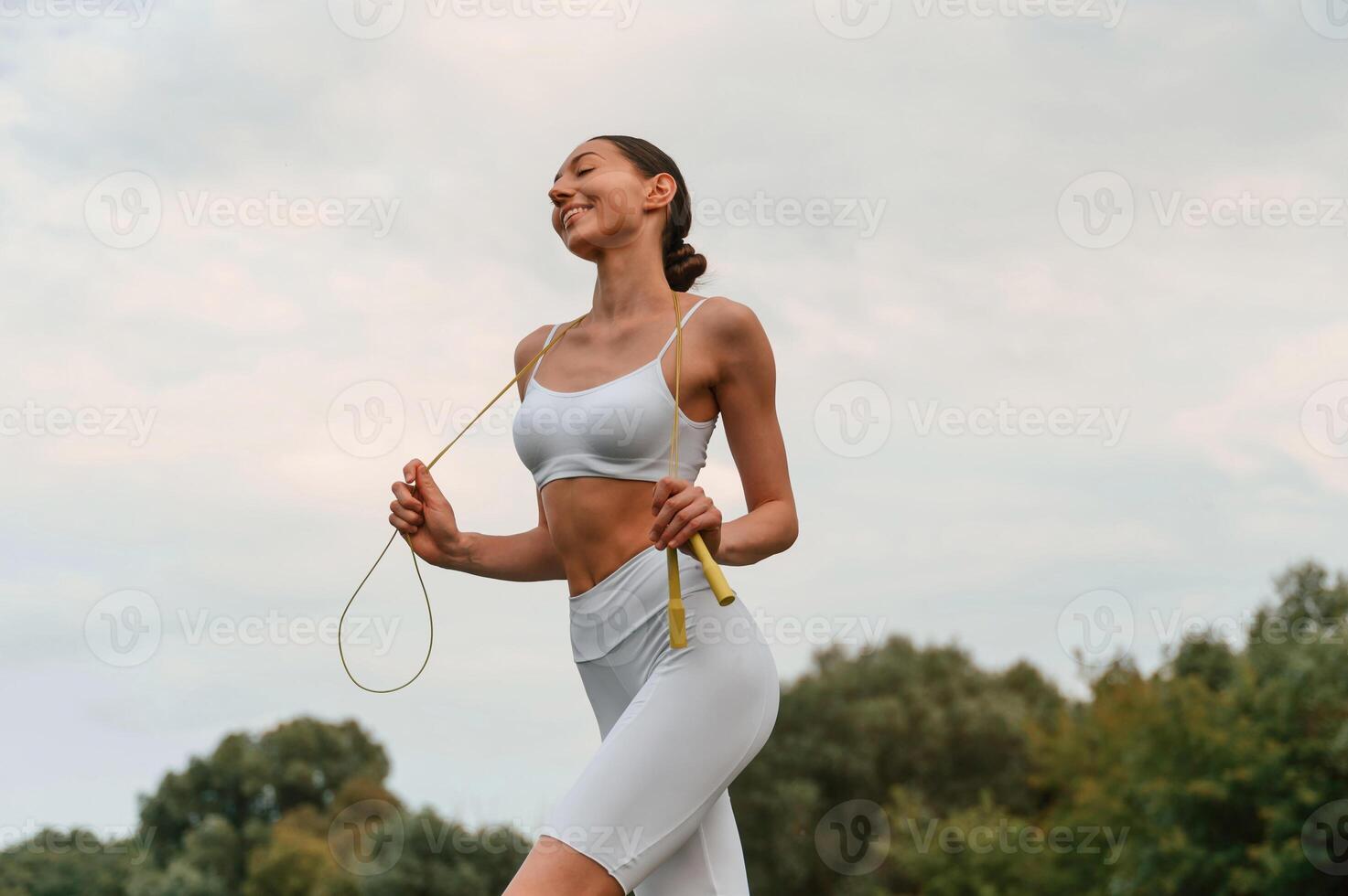 Yellow, colored jumping rope. Young caucasian woman with slim body shape is in the fitness clothes outdoors photo