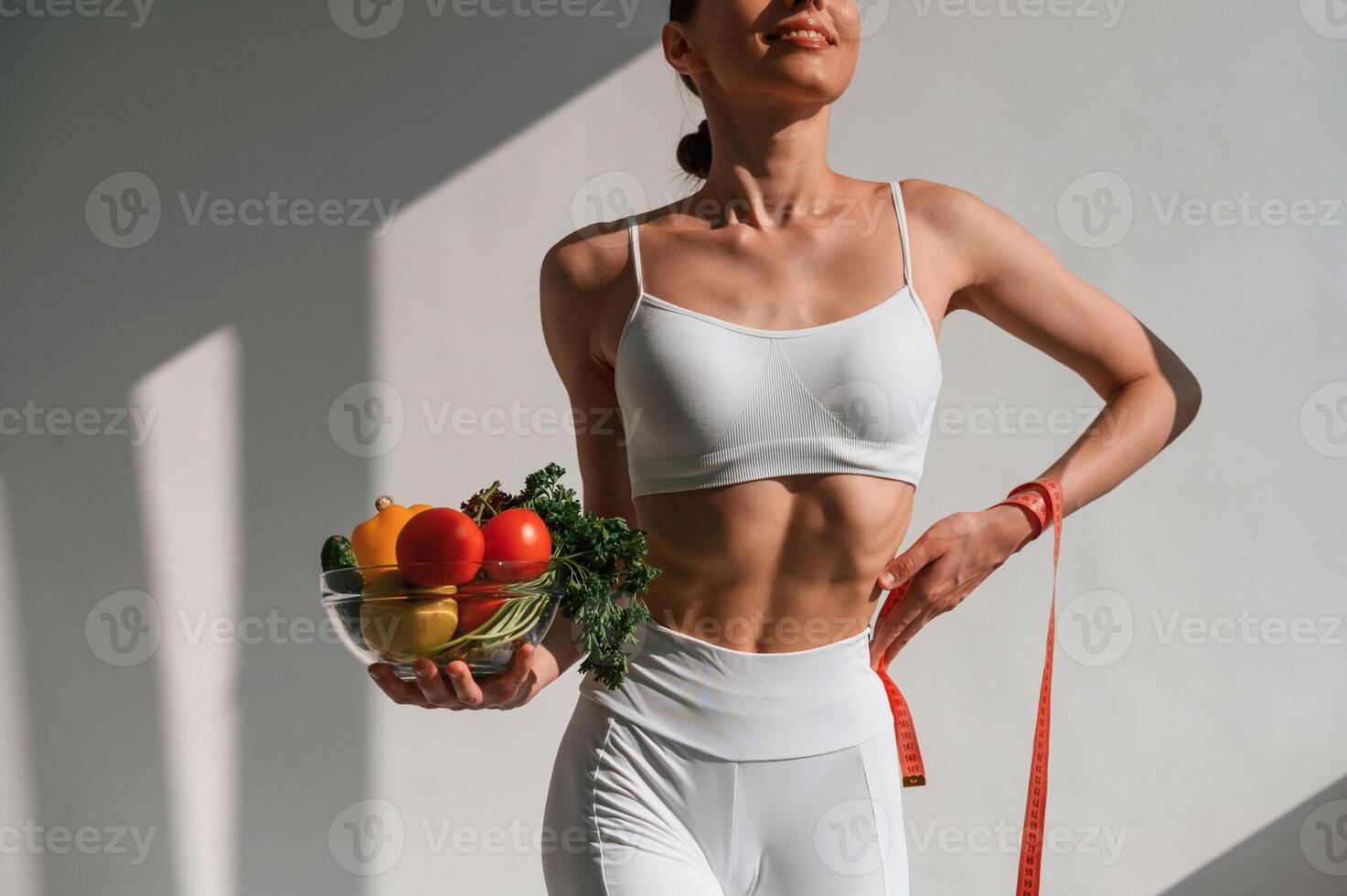 Standing against ,wall, and holding healthy food. Young caucasian woman with slim body shape is indoors in the studio photo