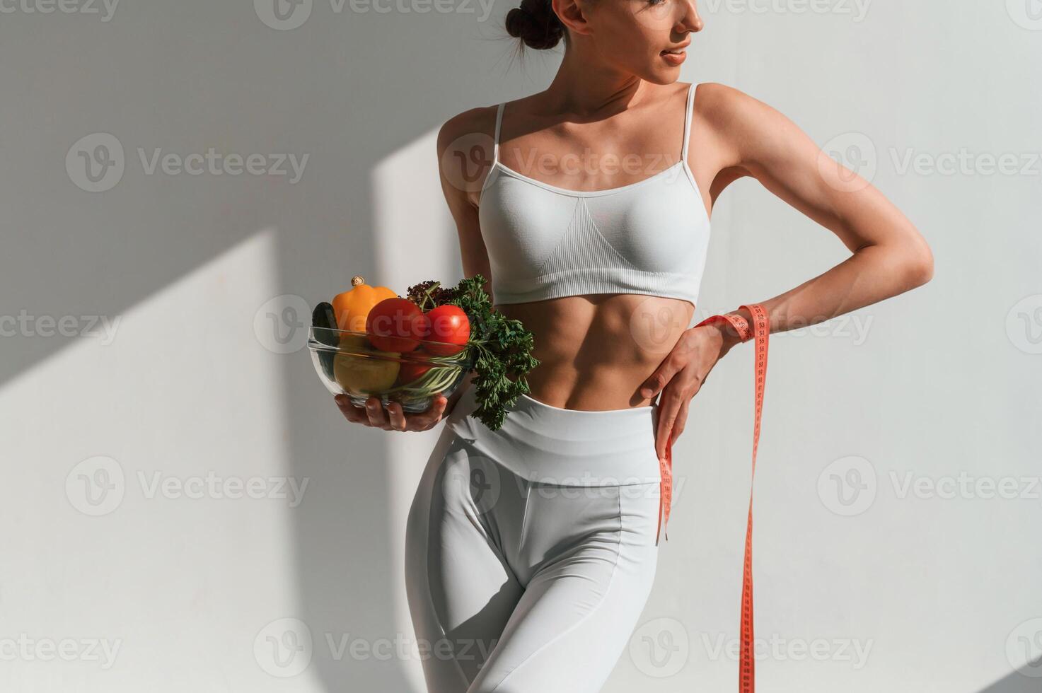 Holding ,a, bowl of vegetables and fruits. Young caucasian woman with slim body shape is indoors in the studio photo