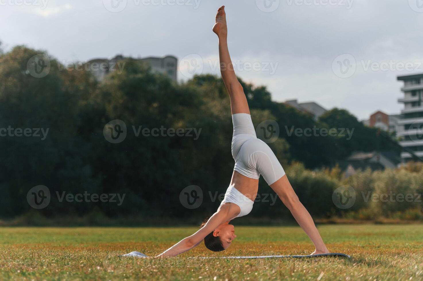 Doing stretching for the legs and spine. Young caucasian woman with slim body shape is in the fitness clothes outdoors photo