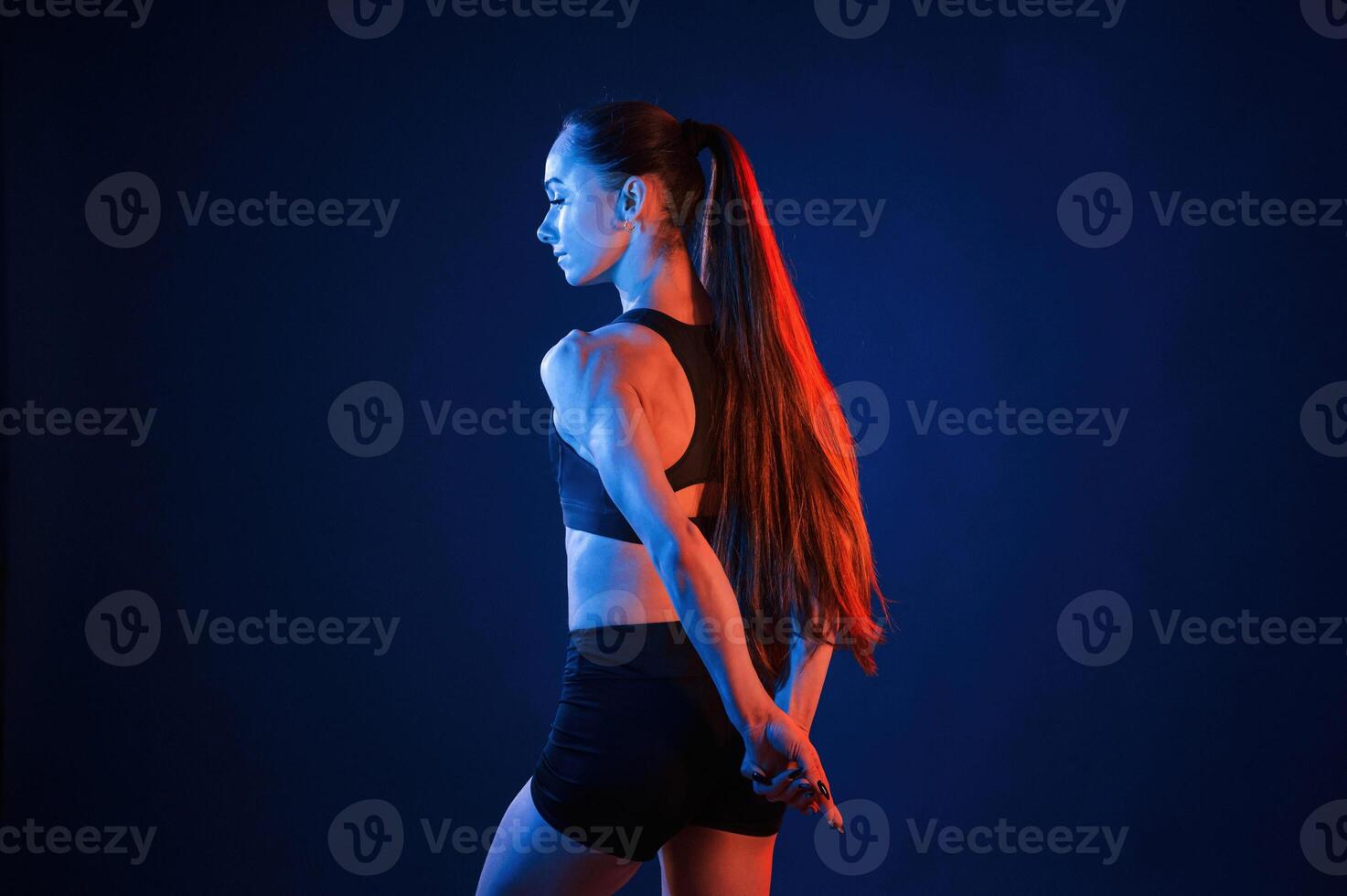Rea,r view. Beautiful muscular woman is indoors in the studio with neon lighting photo