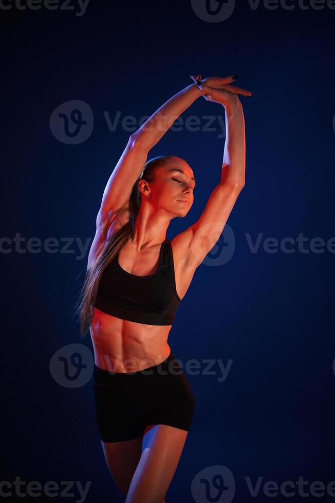 Stretching the hands.. Beautiful muscular woman is indoors in the studio with neon lighting photo