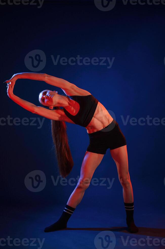 Warm, up exercises. Beautiful muscular woman is indoors in the studio with neon lighting photo