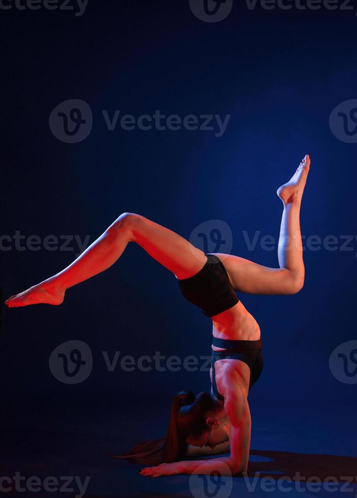 Doing ,hand stand. Beautiful muscular woman is indoors in the studio with neon lighting photo