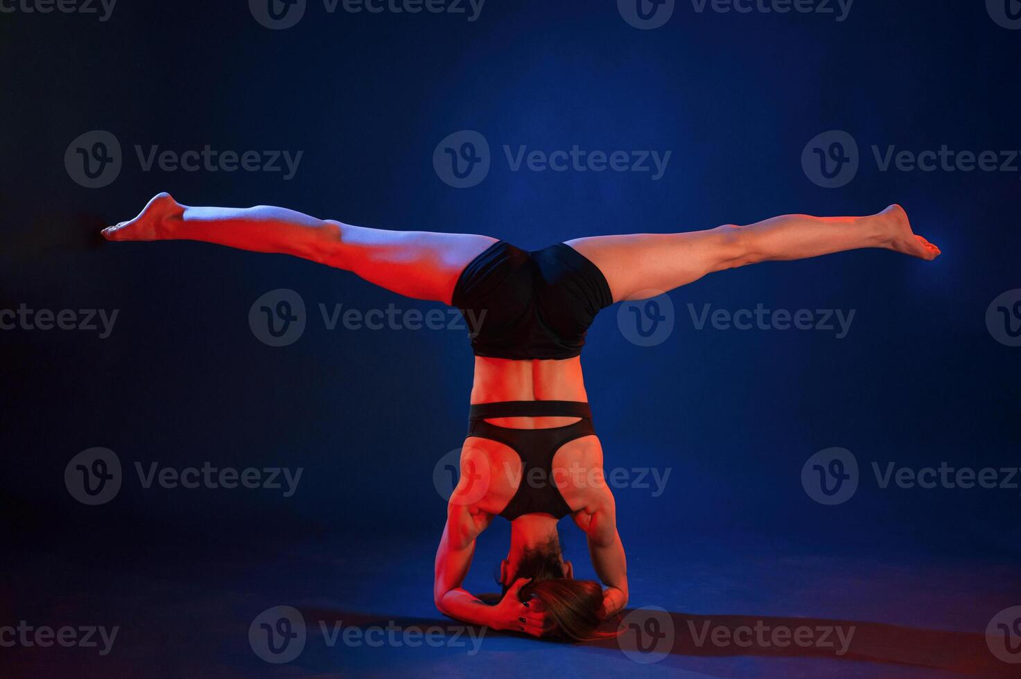 Doing head ,stand. Beautiful muscular woman is indoors in the studio with neon lighting photo