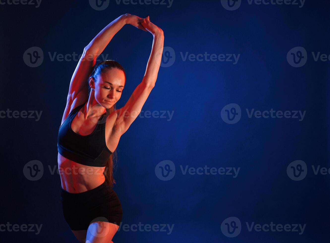 Warm up exercises.. Beautiful muscular woman is indoors in the studio with neon lighting photo